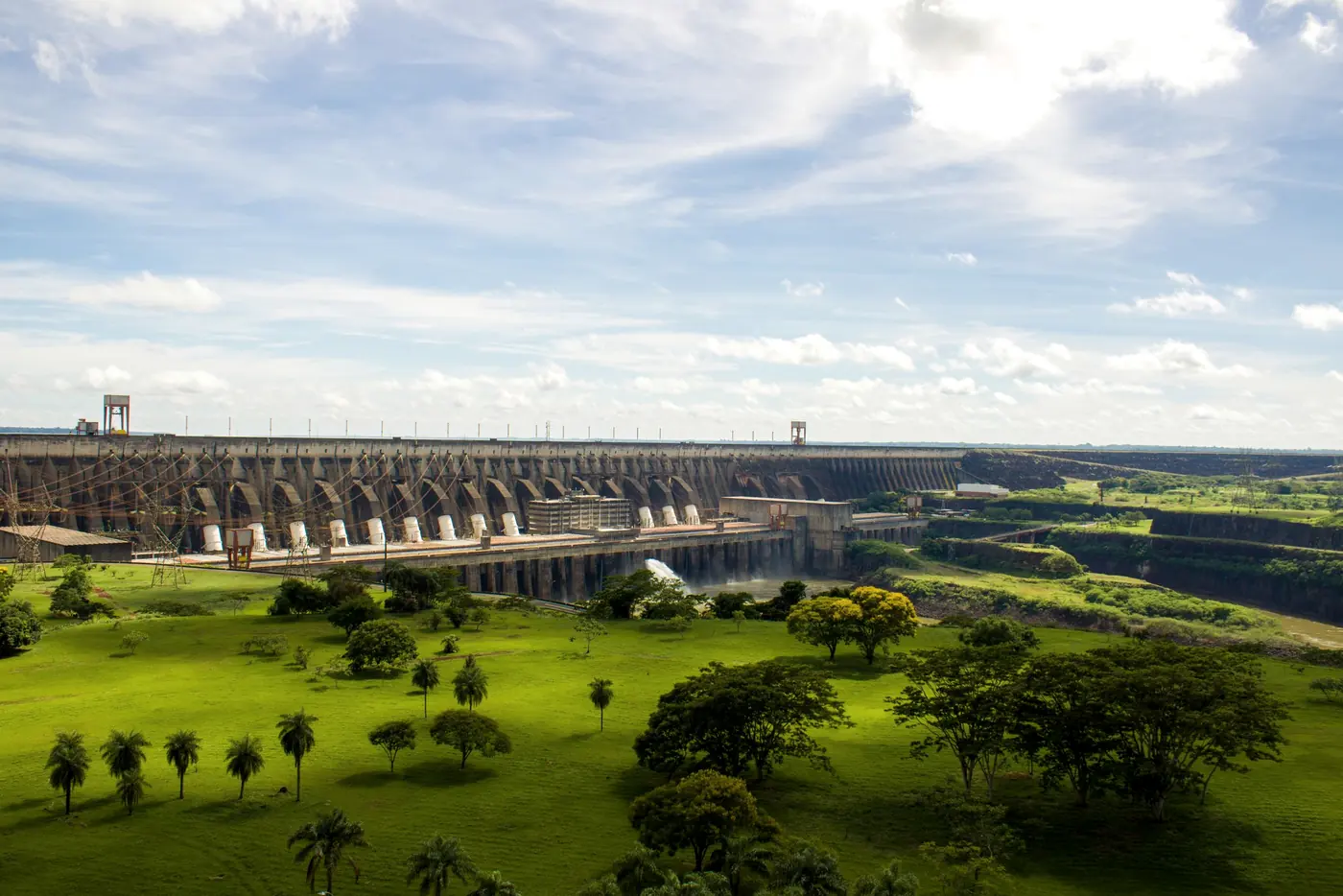 Barramento de usina hidrelétrica visto de longe, com gramado em primeiro plano