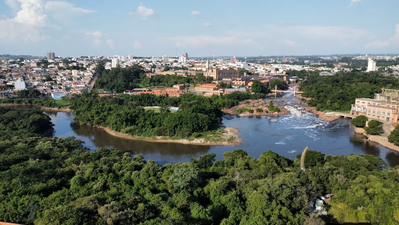 Rio atravessando área urbana, com parque e cidade ao fundo