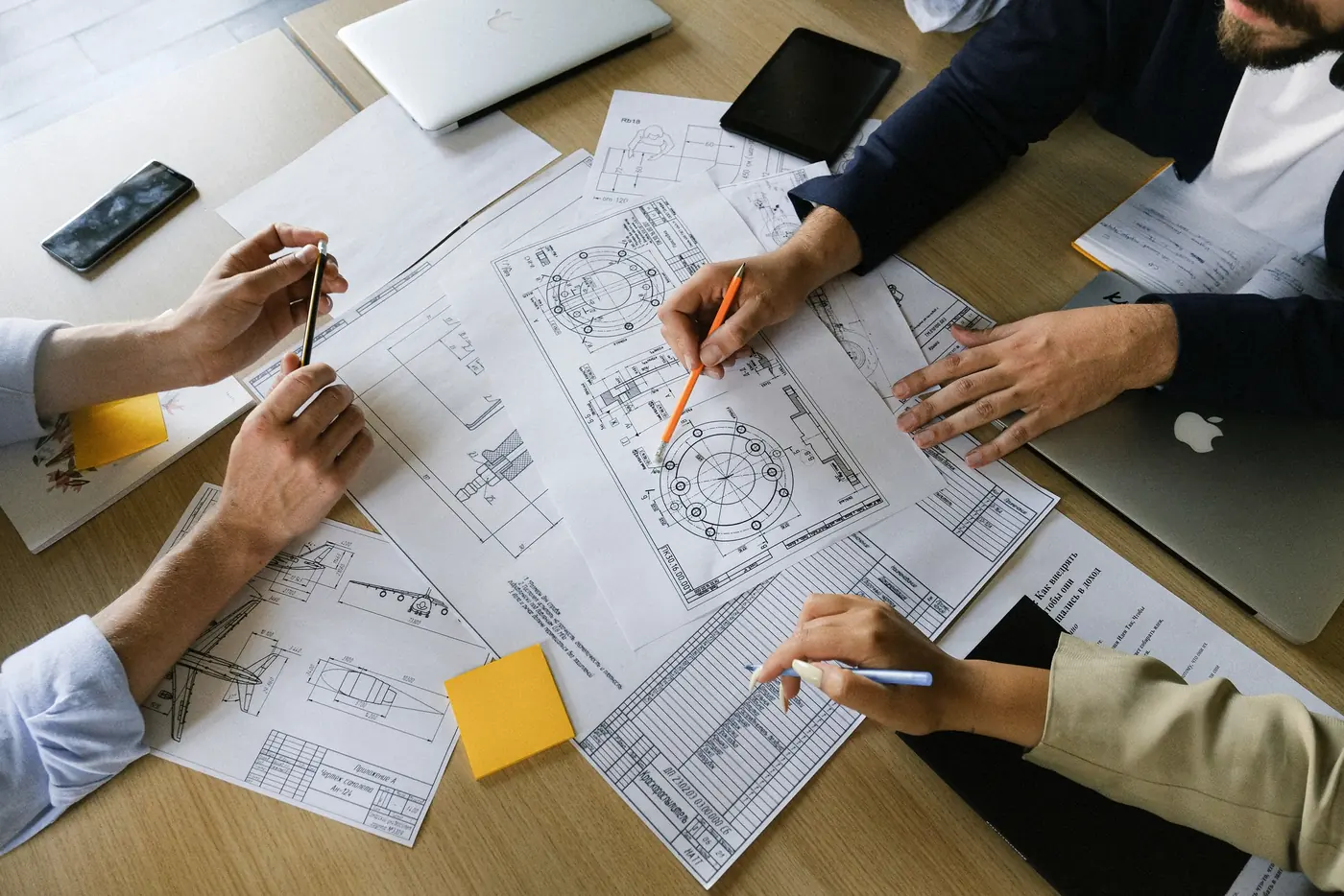 Mãos revisando pranchas de projeto sobre a mesa